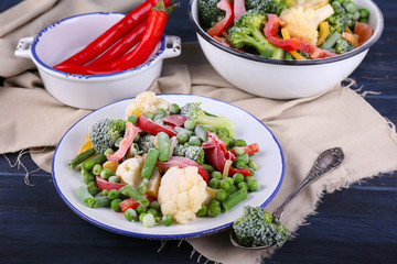 Frozen vegetables on plate on napkin, on wooden table