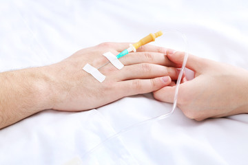 Female hand holding man hand with dropper needle on bed close-up