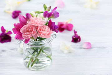 Beautiful spring flowers in glass bottle on wooden background