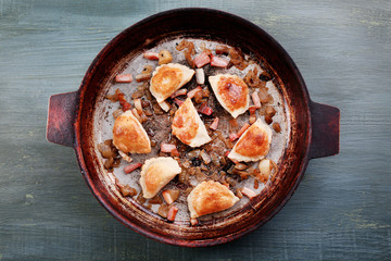 Fried dumplings with onion and bacon in frying pan,