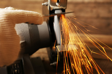 Knife sharpener and hand with blade on wooden table, closeup