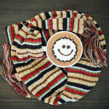 Cup of coffee surrounded the warm scarf on wooden background