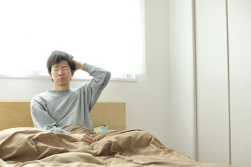 ベッドの上で眠そうにしているパジャマ姿の男性