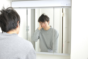 朝起きて自宅の洗面台の鏡に映る眠そうな自分を見つめる日本人男性