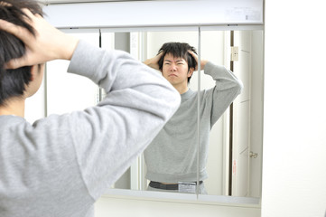 朝起きて自宅の洗面台の鏡に映る眠そうな自分を見つめる日本人男性
