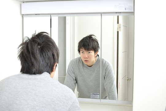 朝起きて自宅の洗面台の鏡に映る眠そうな自分を見つめる日本人男性