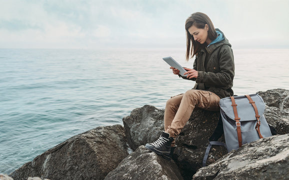 Traveler woman sitting on coast with digital tablet