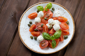 Caprese salad with capers, dark wooden surface, high angle view