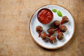 Meatballs in tomato sauce on skewers over rustic wooden surface