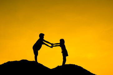 Two children during sun set, holding hands together.