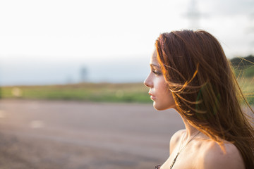 Red-haired young lady standing near the road at sunset