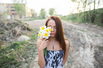 Red-haired young girl with bouquet of daffodils at countryside