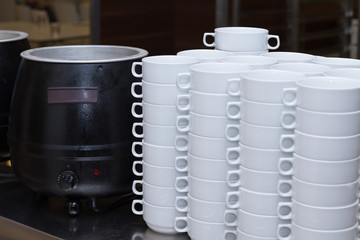 Stack of white soup bowls and soup heater