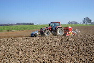 Obraz premium Frühjahrsbestellung, Schlepper mit Sämaschine, Hügellandschaft