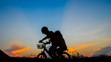 Boy with his sister riding bicycle on sunset background.Silhouet