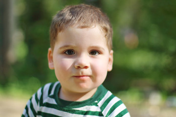 Happy little handsome boy looks at camera in park. Shallow dof
