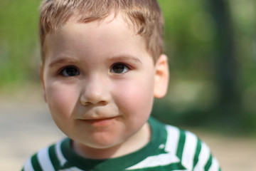 Smiling little cute boy looks at camera in park. Shallow dof