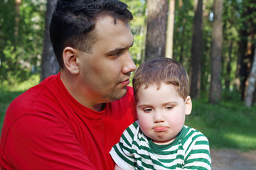 Handsome young father with little cute son sit in summer forest