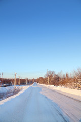 Winter snowy road in small town at sunny day with clear blue sky