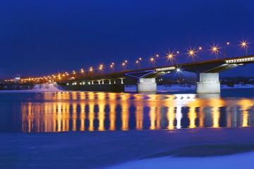 Fototapeta na wymiar Bridge with lanterns and reflection in water of river with ice