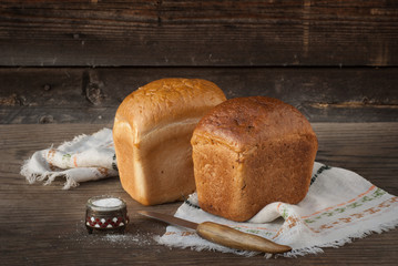 Two loaves of bread, knife, salt lying on a wooden surface