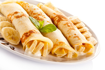 Crepes with bananas and cream on white background