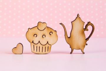 Wooden icons of cake and teapot with little heart on pink backgr
