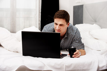 Casual young man using laptop in bed at home.
