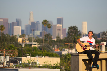 Guitar player on rooftop with Los Angeles skyline in background
