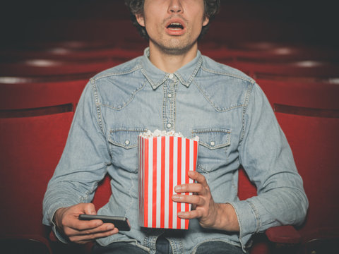Man in cinema watching movie and using his phone