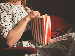 Young woman eating popcorn in movie theater - obrazy, fototapety, plakaty