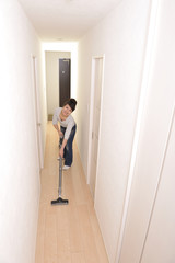 Fototapeta premium 笑顔でマンションの部屋に掃除機をかけているアジア人の綺麗な女性