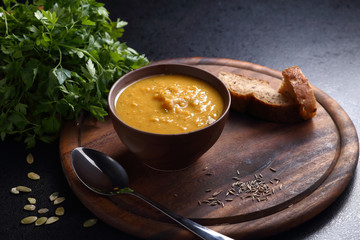 Pumpkin and lentil soup, bread and green on the wooden board