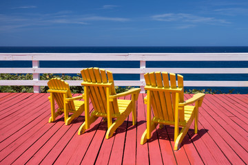 adirondack chairs on a red deck at ocean