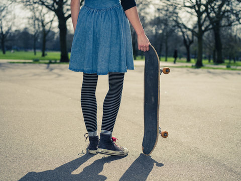 Young woman standing in the park with a skateboard
