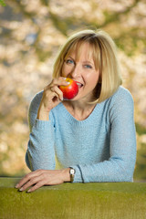 atrractive mature woman is biting in an apple