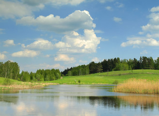 Green spring landscape with lake and rolling hills, fields, and forest. The image represents nature, countryside, tranquility, and sustainable rural environment.
