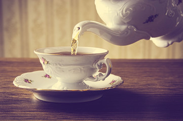 Old-fashioned pouring tea to cup on old wallpaper background
