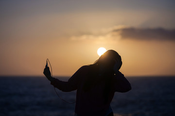 young girl with headphones and smart phone at the beach