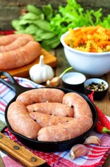 raw chicken sausages with vegetables on a frying pan