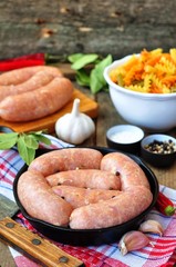 raw chicken sausages with vegetables on a frying pan
