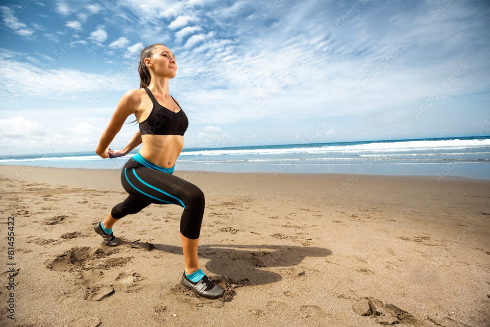 Wall mural young woman stretching on beach