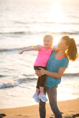 Healthy mother and baby girl pointing while on beach