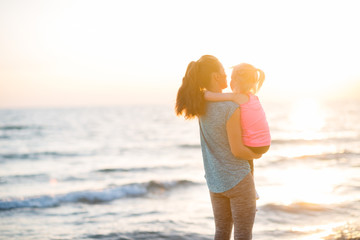Healthy mother and baby girl looking into distance on beach