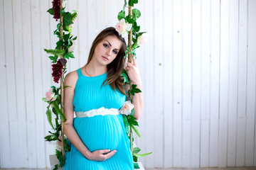 Fototapeta premium Portrait of a pregnant woman on a swing in the room