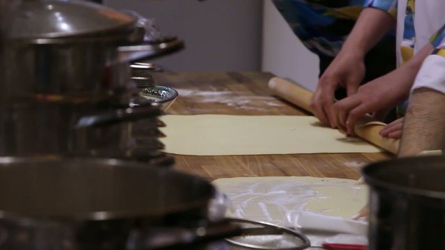 Chefs hands unrolling dough with a rolling pin in kitchen