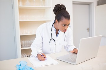 Scientist taking notes while using laptop