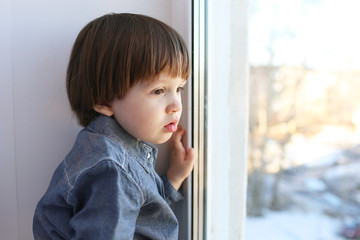 Sad little boy looks out of window