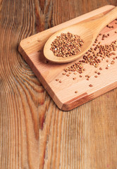 Dry buckwheat in a spoon on a wooden cutting board