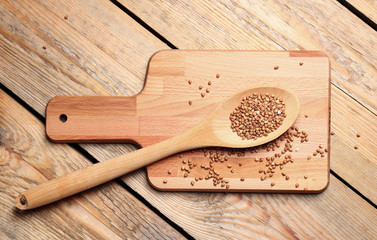 Dry buckwheat in a spoon on a wooden cutting board